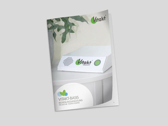 Bedienungsanleitung f&uuml;r Vitakt-Basis auf einem Tisch mit einer Pflanze im Hintergrund.