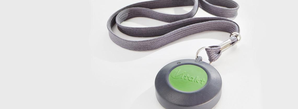 Runder, grauer Schl&uuml;sselanh&auml;nger mit gr&uuml;ner Fl&auml;che und Aufschrift "Vitakt" an grauem Textilband.